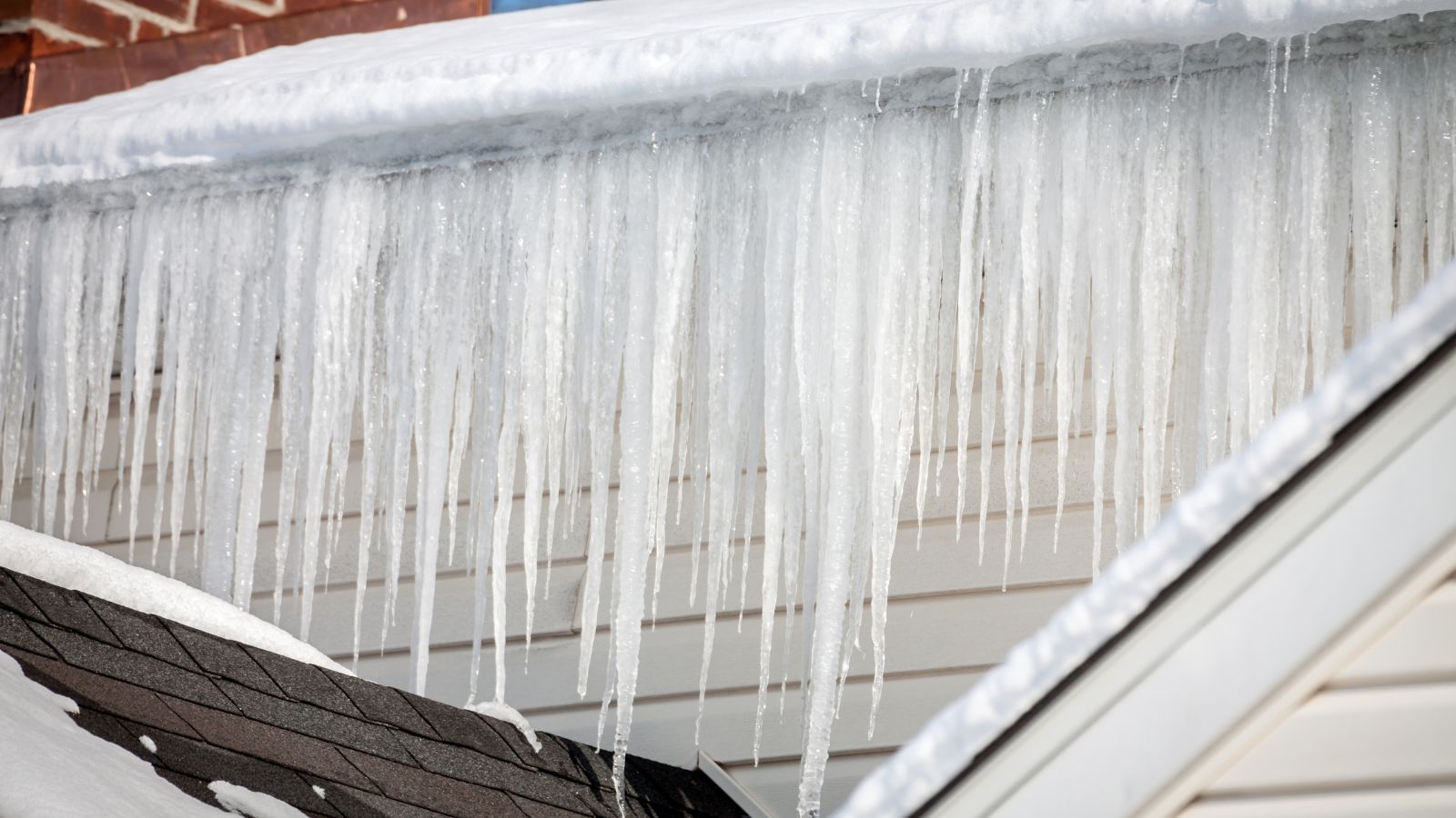 Ice dam with large icicles forming along roof edge during winter thaw in Central New York